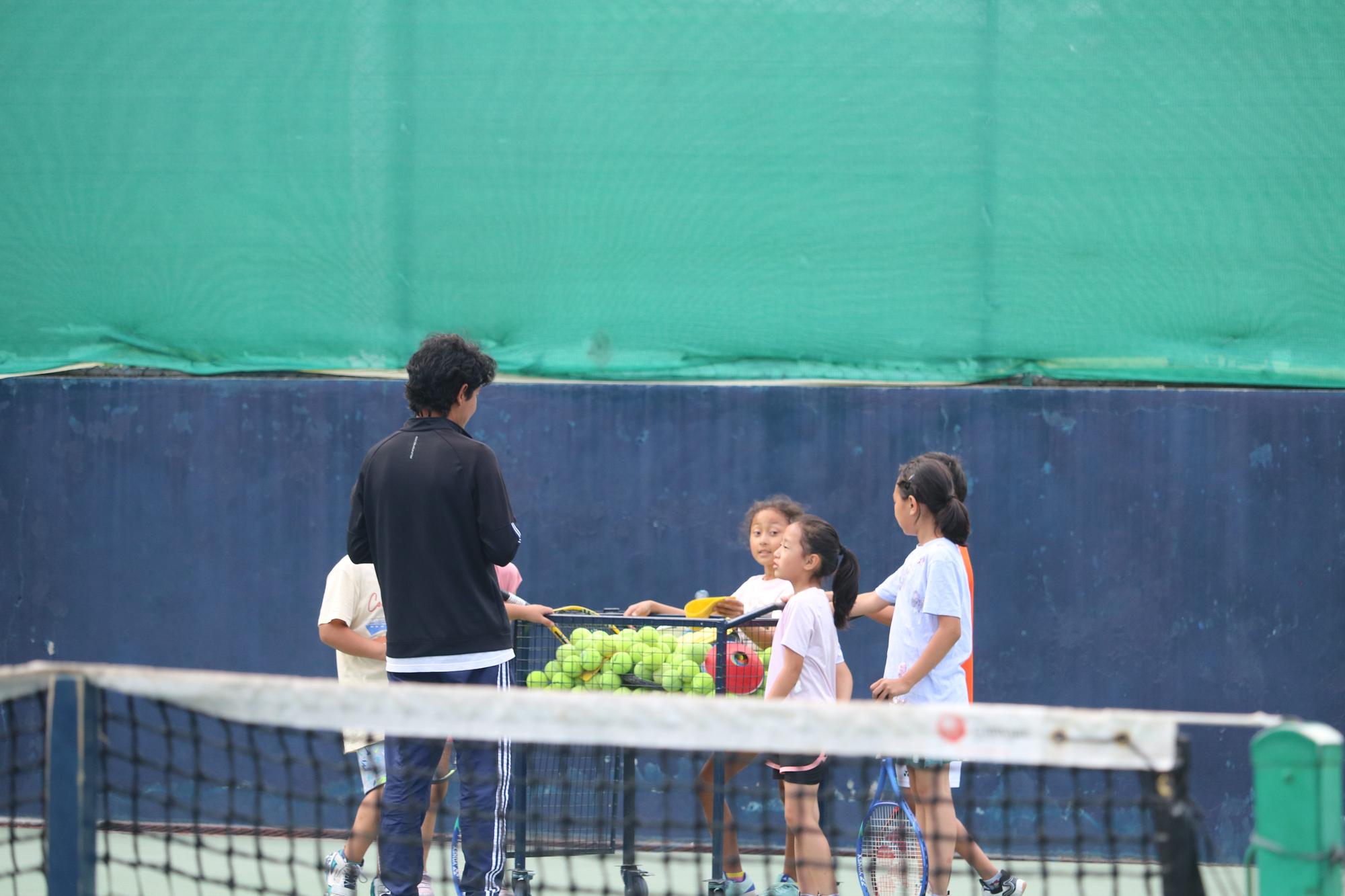 A coach working with young players beside a basket of balls