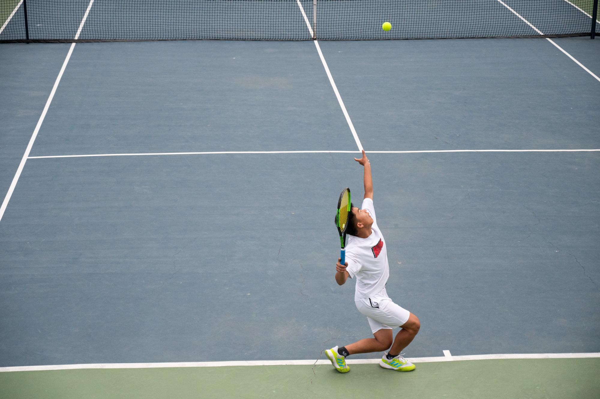 A young Bhutanese player reaching up to serve on the hard courts at Changlimithang