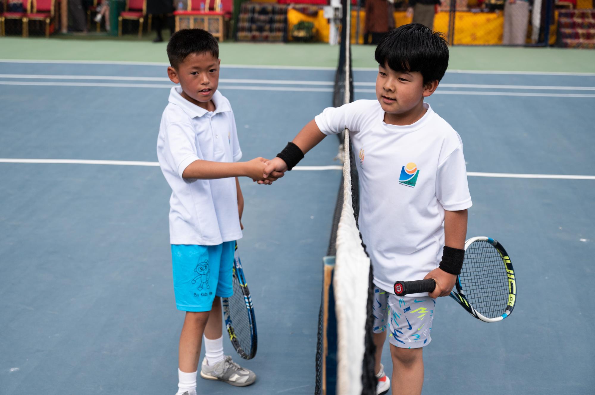 Two junior players shaking hands over the net after a match